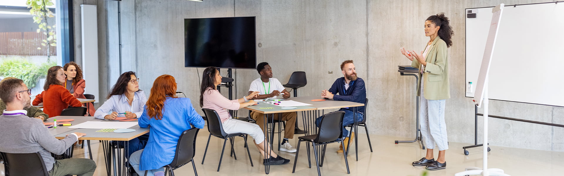 A group of people attending a seminar being led by a woman next to a whiteboard